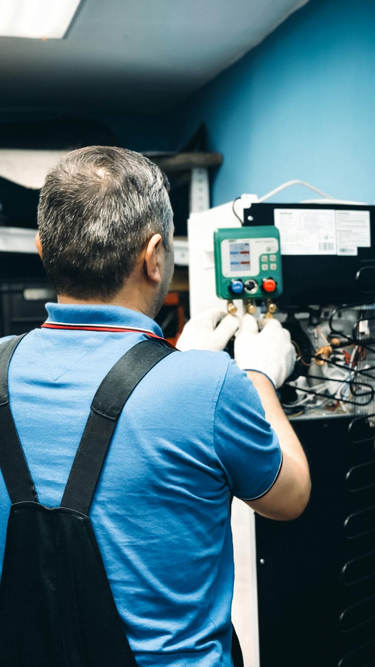 Technician working on refrigeration equipment with gauges in a utility room.